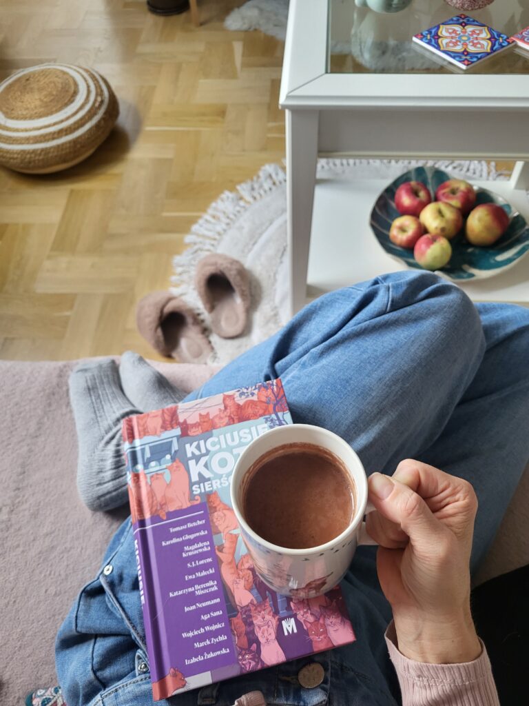 Tytułowa książka w ręku i czarno-biały pies zerkający w stronę książki.