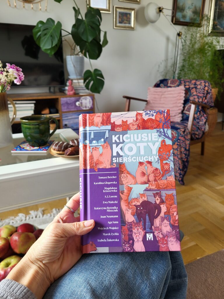 Tytułowa książka w ręku, w tle wnętrze salonu.